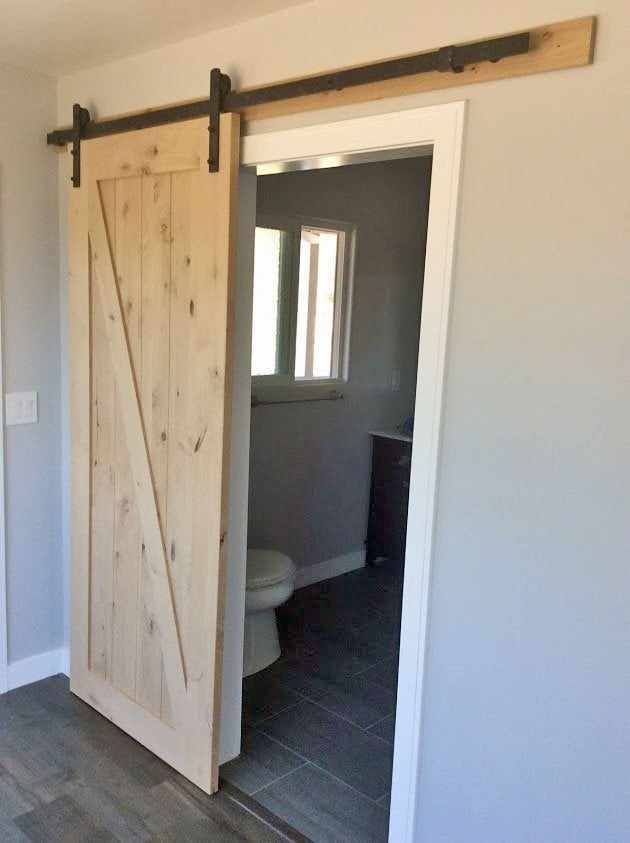 Wood barn door on a sliding rail, partly closed in front of a bathroom