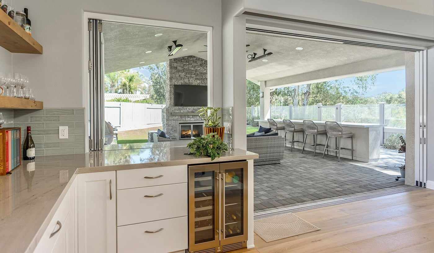Folding glass doors fully open between a kitchen bar and a covered patio