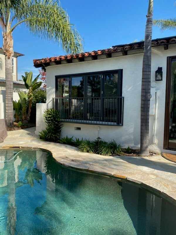 Folding doors with a railing on a stucco pool house with a tile roof in San Diego