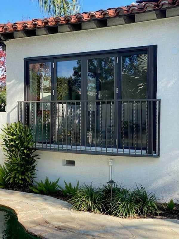 Dark-framed folding doors with a railing on the white stucco wall of a San Diego home, under a tile roof