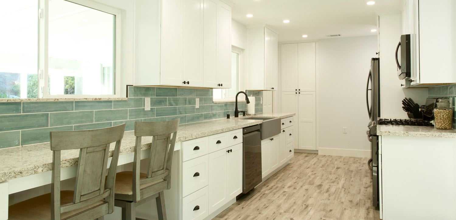 Home improvement project: a remodeled white kitchen with a green tile backsplash and a built-in desk