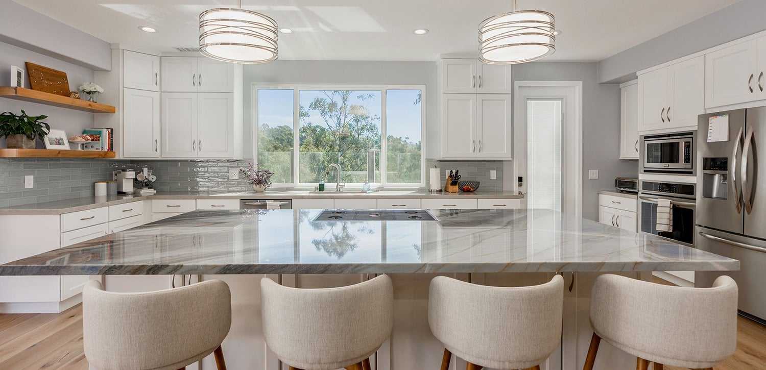Remodeled kitchen with white cabinets, a large marble-look island, pendant lights and bar stools