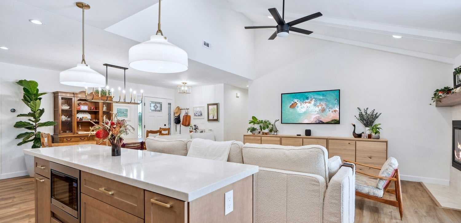 Kitchen and living room opened into one space after a wall was removed, with a white island and pendant lights