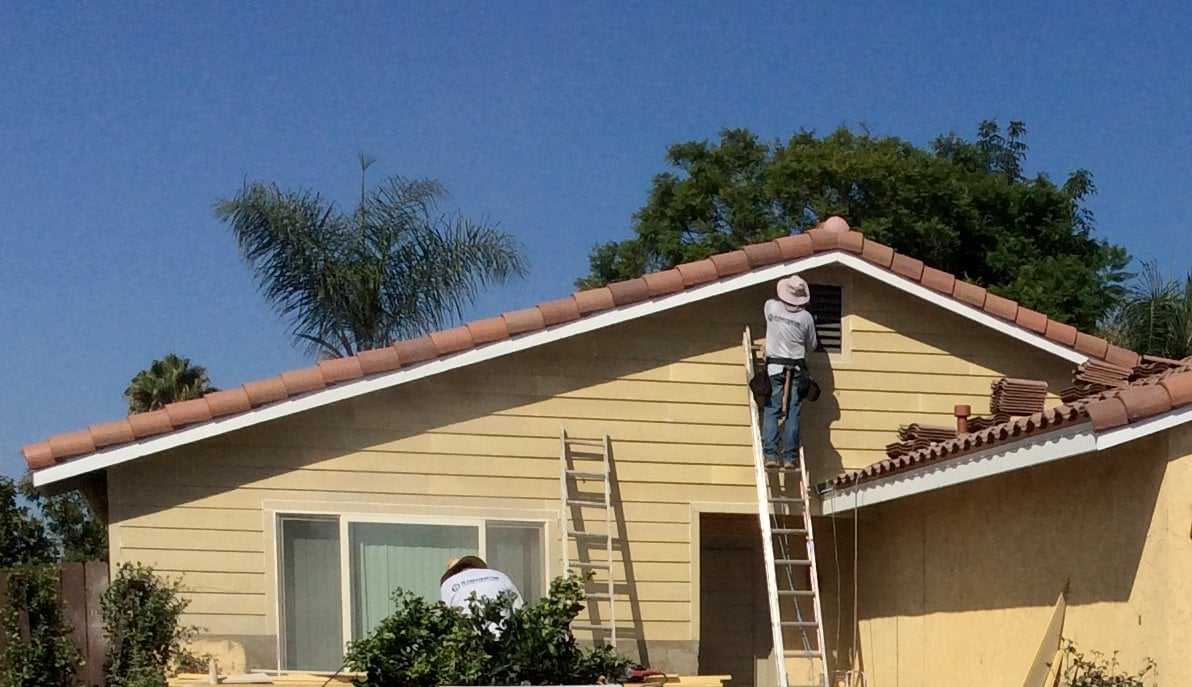 Worker on a ladder installing new siding on a single-story house