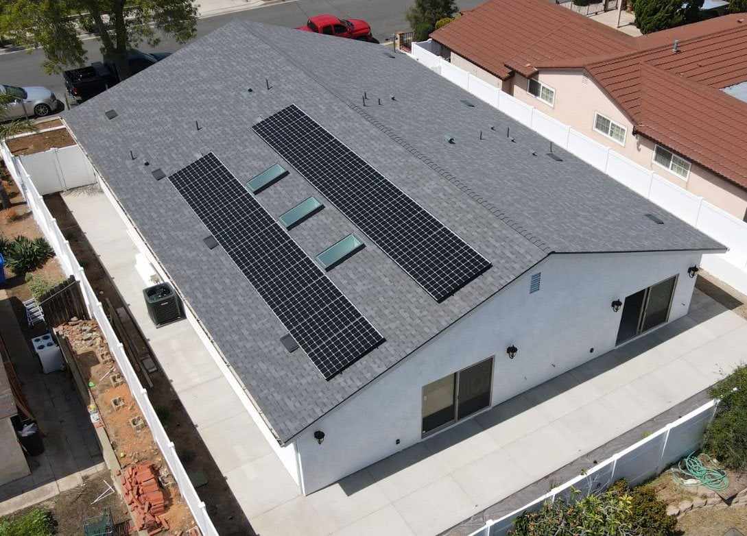 Aerial view of two rows of solar panels on the gray shingle roof of a Clairemont home, with skylights