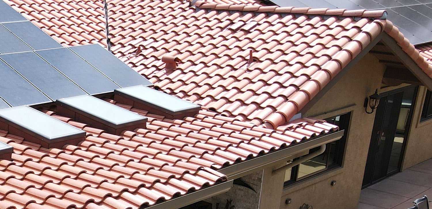 Solar panels installed on a red clay tile roof, beside skylights