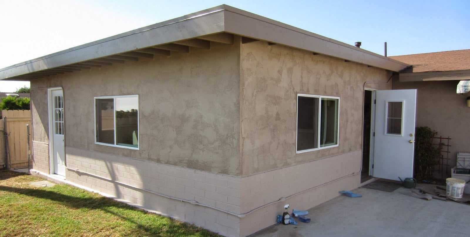 Stucco sunroom addition with windows and a side door on the back of a house