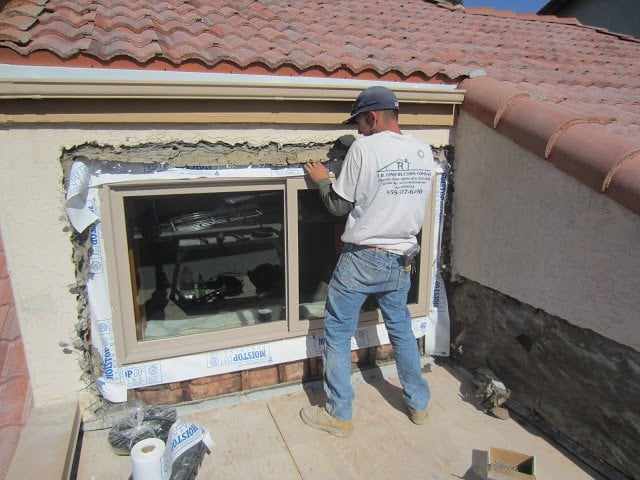 TR Construction installer setting a new window into the stucco wall of a San Diego home under a tile roof